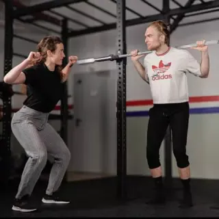 Eine Trainerin zeigt einem Mann, die Ausführung beim squatten mit Gewichten.