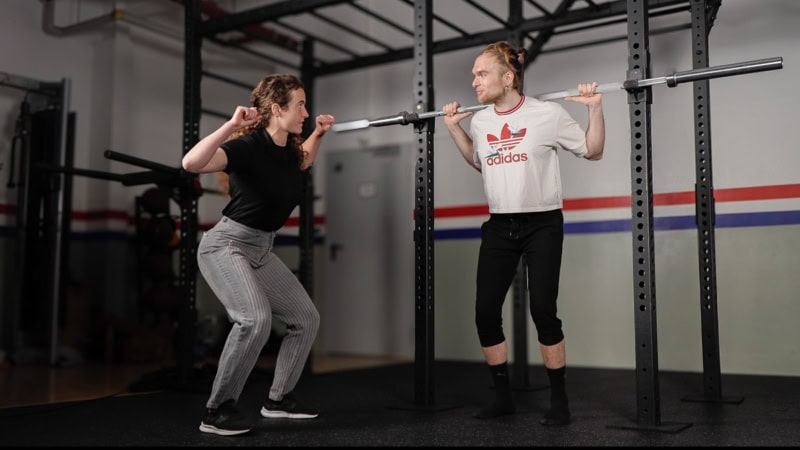 Eine Trainerin zeigt einem Mann, die Ausführung beim squatten mit Gewichten.