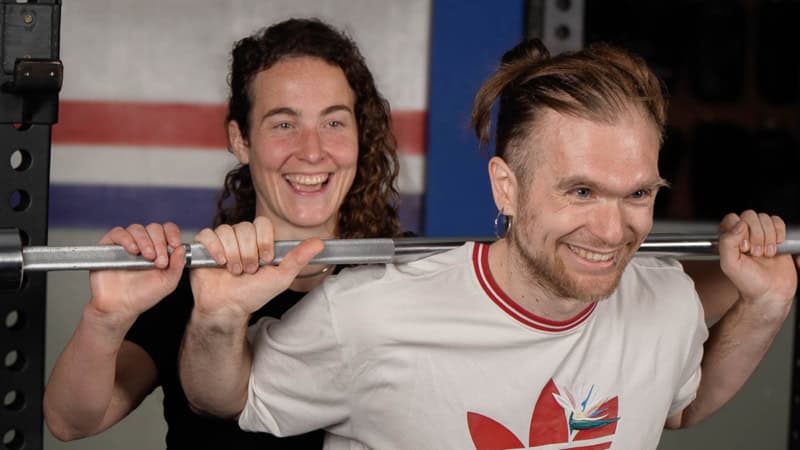 Eine Trainerin unterstützt einen Mann beim squatten.