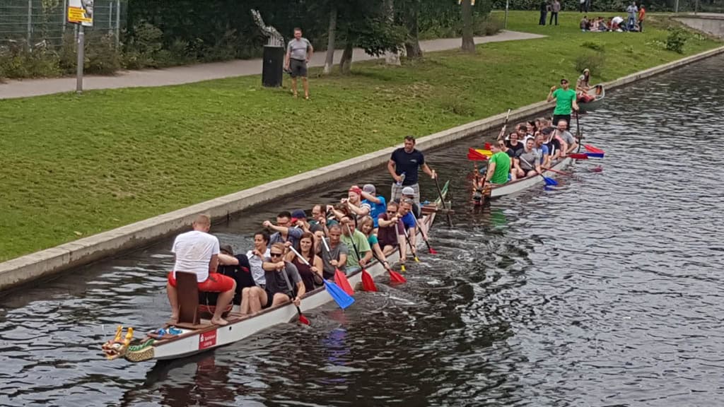Zwei Drachenboote auf einem Kanal, vollbesetzt mit Ruderern.