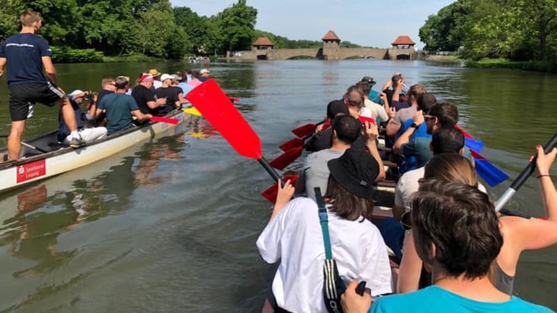 Zwei Drachenboote auf gemütlicher Fahrt in einer Breiten Wasserstraße mit Blick auf eine Historische Brücke.