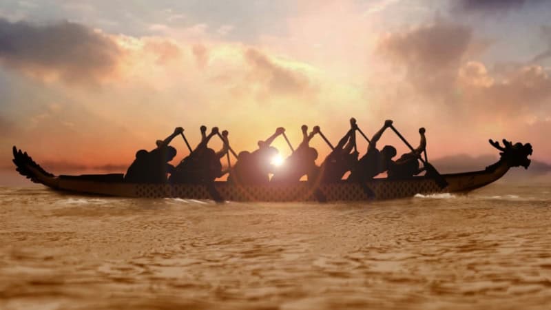 Ein Drachenboot was über eine See bei Sonnenuntergang fährt.