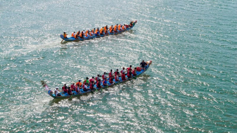 2 große Drachenboote fahren über einen breiten Fluss