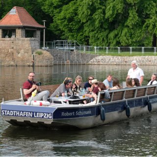 Motorboot auf ruhiger Fahrt durch einem Leipziger Kanal mit einer Gruppe Menschen.