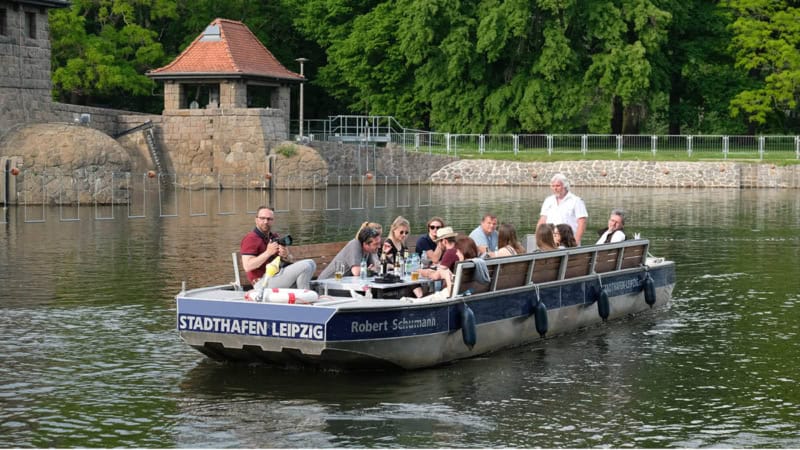 Motorboot auf ruhiger Fahrt durch einem Leipziger Kanal mit einer Gruppe Menschen.