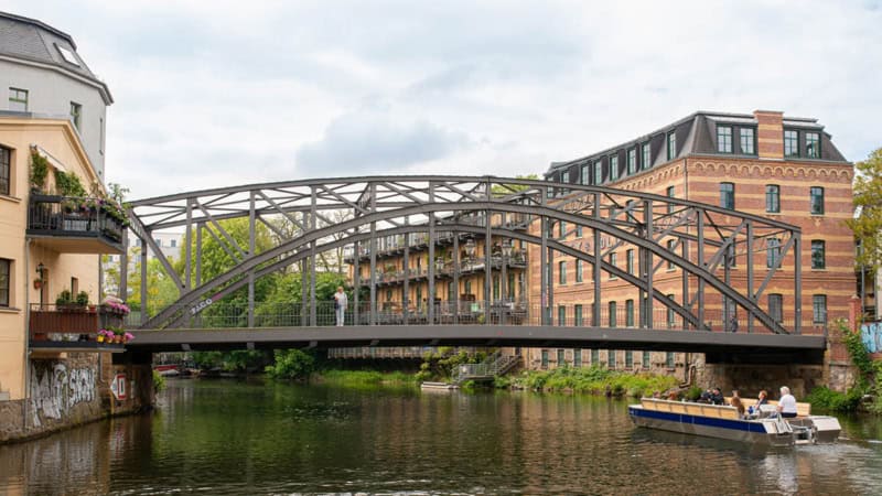 Motorboot fährt durch einen Kanal in Leipzig unter einer Brücke entlang.
