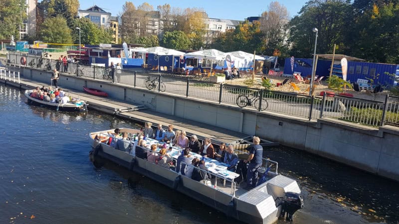 Motorboot an einer Anlegestelle in Leipzig mit Blick auf eine Strandbar.