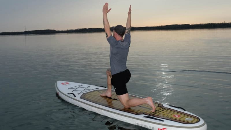 Mann macht Yoga auf stand up paddle im Sonnenuntergang auf einem See