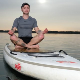 ein Mann meditier auf seinem stand up paddle auf einem See