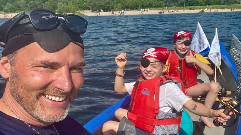 ein Mann und 2 Kinder die als Piraten verkleidet sind fahren in einem Kajak auf einem See