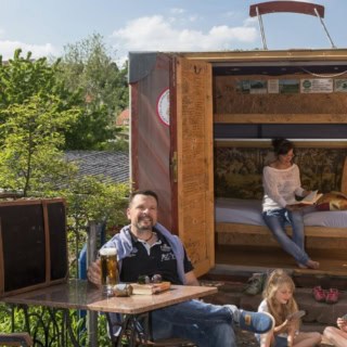 Familie sitzt glücklich vor dem Kofferhotel mit einem Bier auf den Tisch