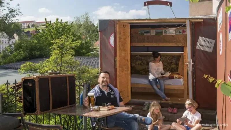 Familie sitzt glücklich vor dem Kofferhotel mit einem Bier auf den Tisch