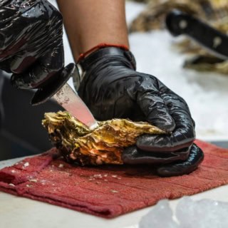 Ein Teilnehmer des Kochkurses öffnet mit einem Messer eine Auster.