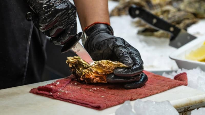 Ein Teilnehmer des Kochkurses öffnet mit einem Messer eine Auster.