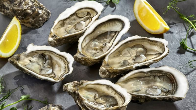 Sieben Austern liegen auf eine Servierplatte mit Zitronen - Kochkurs.
