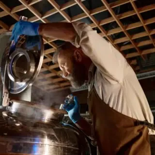 Ein Mann kontrolliert das gebraute Bier in einem Kessel.