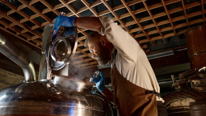 Ein Mann kontrolliert das gebraute Bier in einem Kessel.