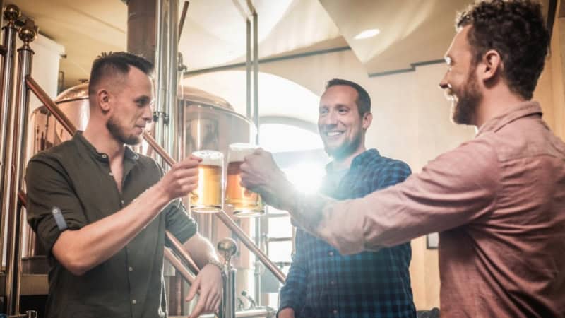 Drei Männer stoßen mit selbstgebrautem Bier an.