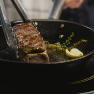 Die Seite eines Steaks wird in einer Pfanne angebraten.