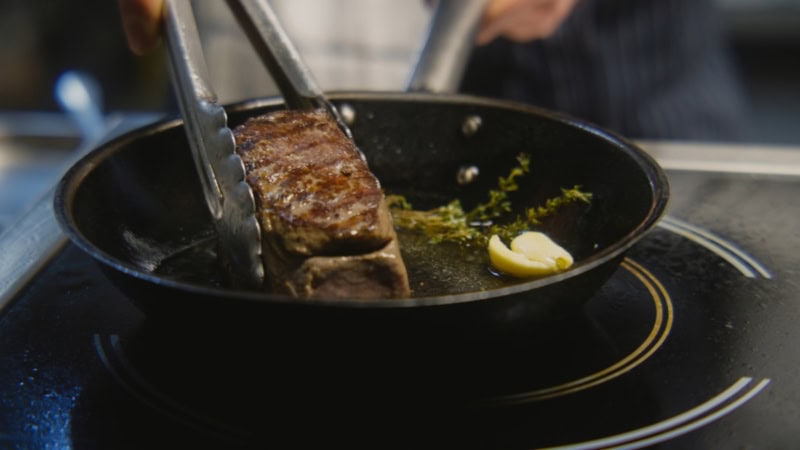 Die Seite eines Steaks wird in einer Pfanne angebraten.