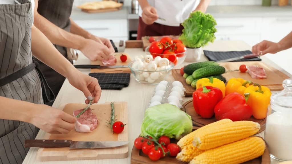 Kochkurs-Fleisch-vorbereiten Vier Köche reiben ein vor sich liegendes Steak mit Thymian ein.