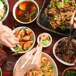 Kochkurs-asiatisch-essen Verschiedene asiatische Gerichte stehen auf einem Tisch von dem sich Menschen mit Stäbchen bedienen.