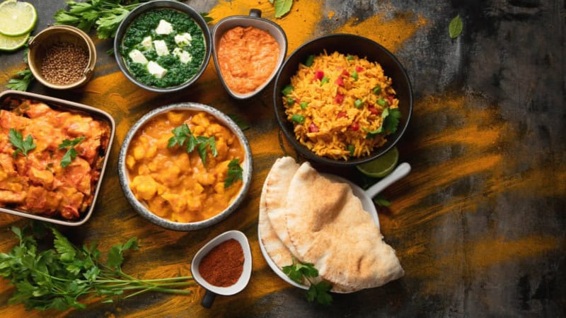 Indisches Curry, Indisches Fladenbrot und Reis sind mit Beilagen auf einem Tisch aufgetischt.