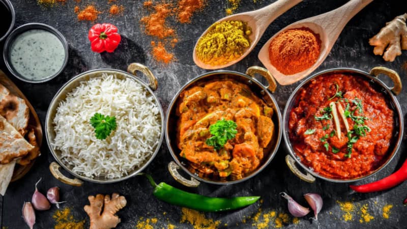 Ein rotes und ein gelbes Currygericht sind in Töpfen mit Reis aufgetischt.