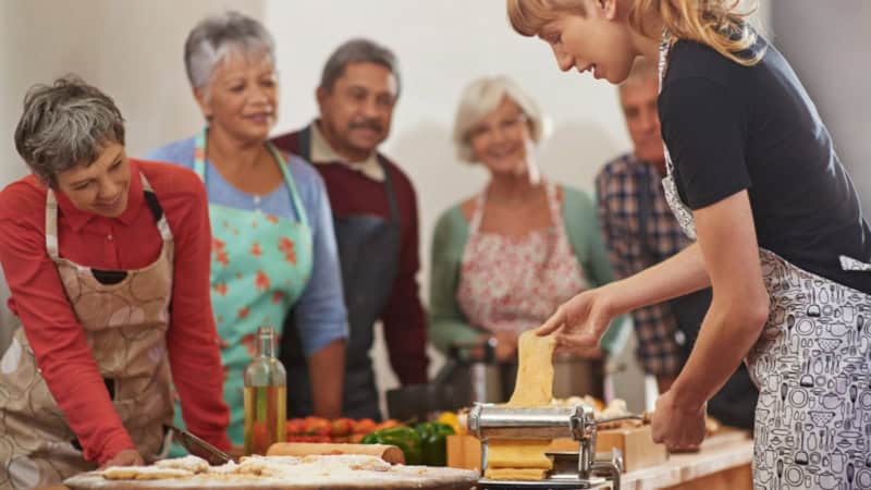 Eine Köchin plättet Nudelteil während die Kochkursteilnehmer zusehen.