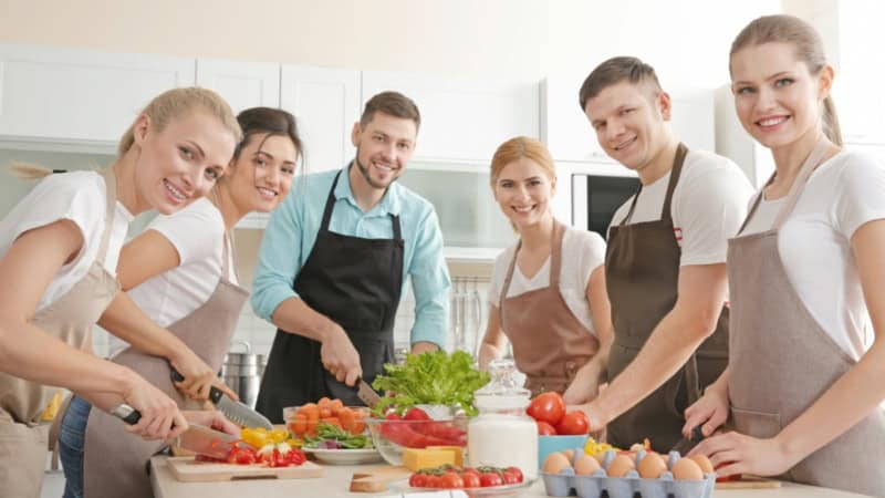 Eine Gruppe Kochkursteilnehmer die Gemüse schneidet.