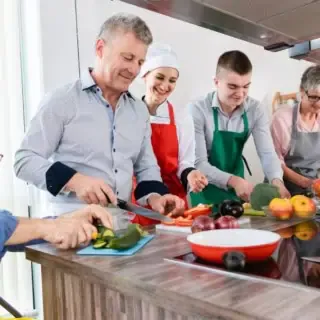 Eine Gruppe Kochkursteilnehmer die Gemüse schneidet.