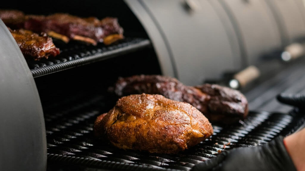 Kochkurs-smoker-fleisch-entnehmen Eine Fleischplatte wird in den Smoker geschoben.