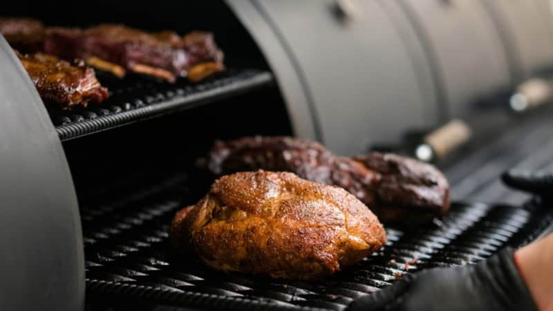 Eine Fleischplatte wird in den Smoker geschoben.