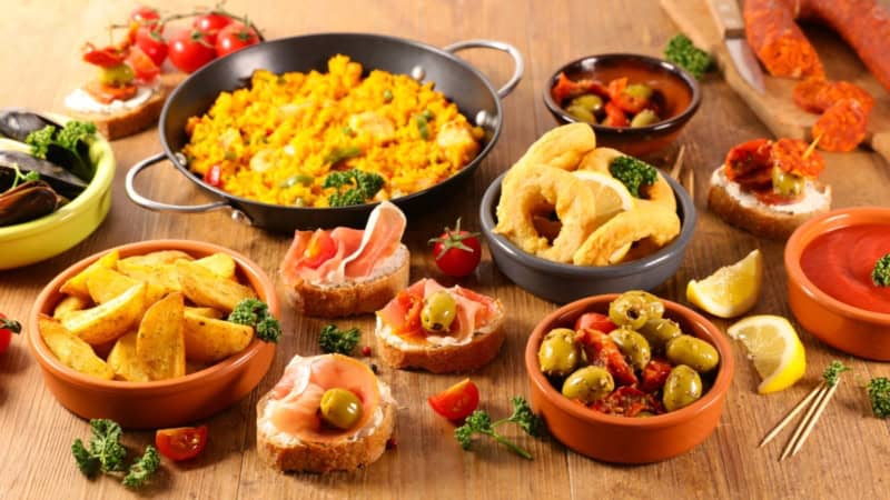 Frittierte Tintenfischringe, Ofenkartoffeln, Oliven und weitere Tapas auf einem Tisch angerichtet.