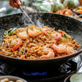 Ein thailändisches Nudelgericht, welches mit Meeresfrüchten in einem Wok angebraten wird.