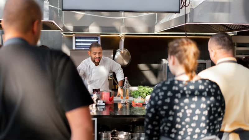 Ein Koch erklärt Kochkursteilnehmern etwas.