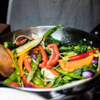 Verschiedenes Gemüse wird in einer Stahlpfanne angebraten.
