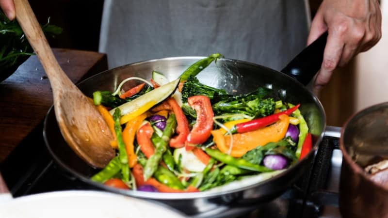 Verschiedenes Gemüse wird in einer Stahlpfanne angebraten.