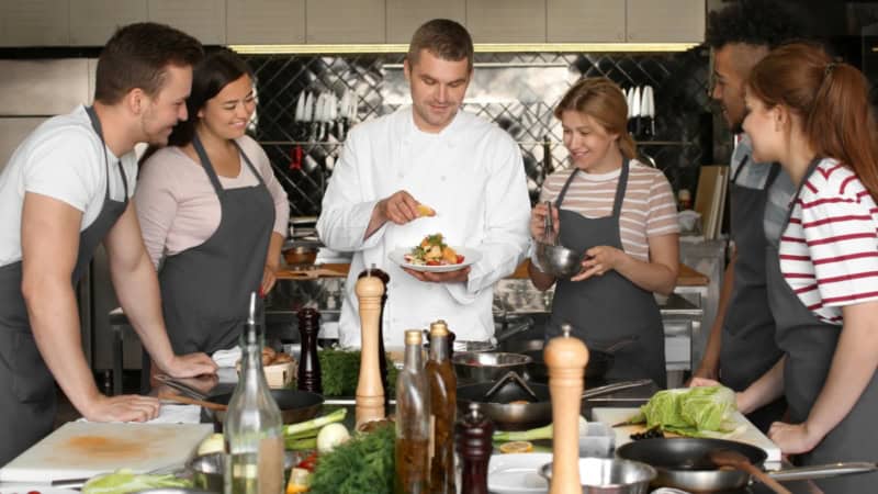 Ein Kochlehrer der den Kochkursteilnehmern etwas erklärt.
