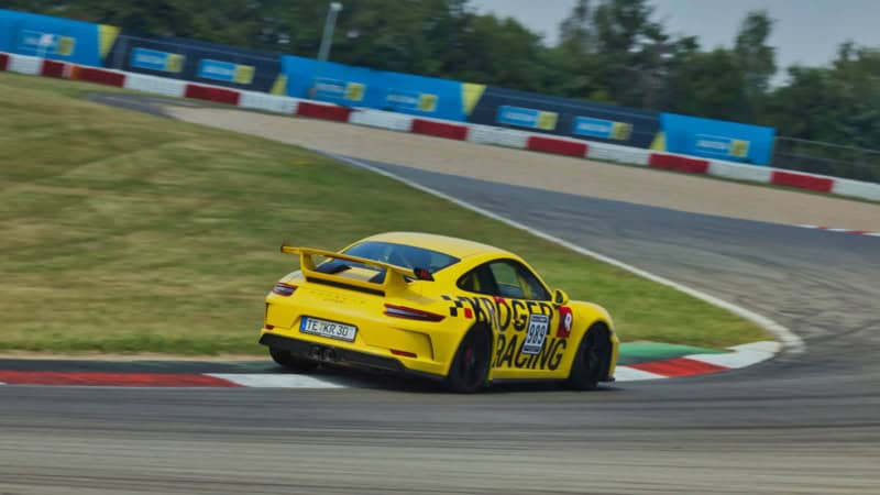 Ein gelber Porsche GT3 MR fährt in auf einer Rennstrecke in eine Kurve.