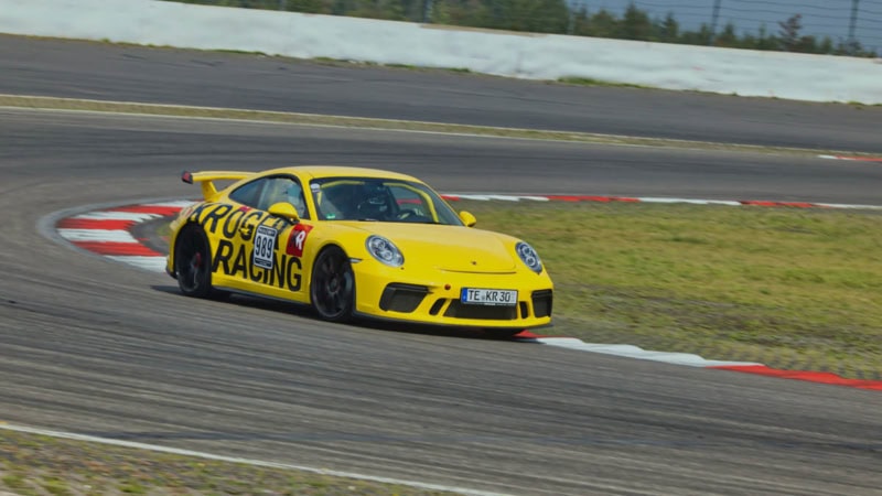 Ein gelber Porsche GT3 MR fährt aus einer Kurve heraus.