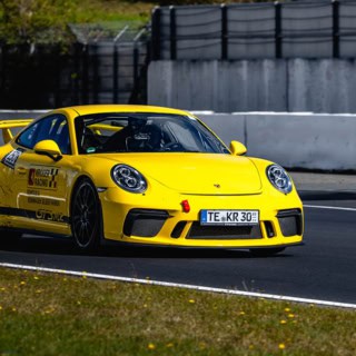 Frontale Aufnahme eines gelben Porsche GT3 MR auf einer Rennstrecke.