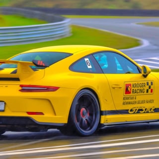 Nahaufnahme eines gelben Porsche GT3 MR von hinten, während das Auto auf einer Rennstrecke fährt.