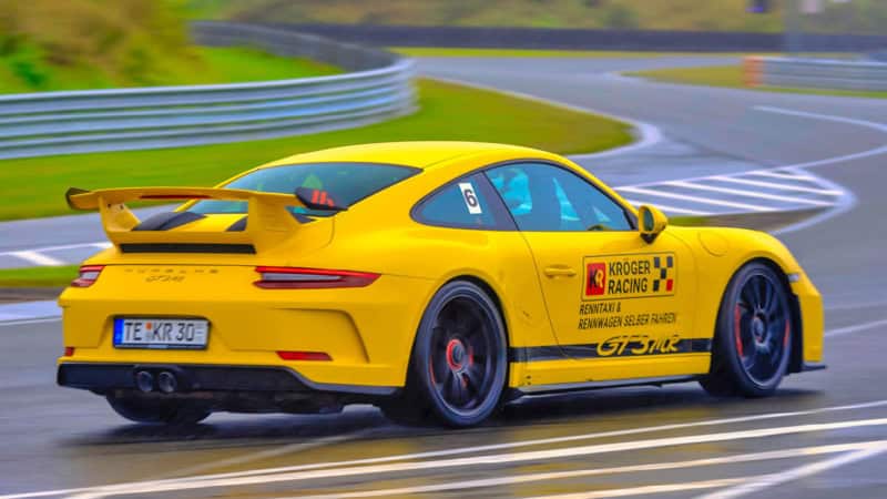 Nahaufnahme eines gelben Porsche GT3 MR von hinten, während das Auto auf einer Rennstrecke fährt.