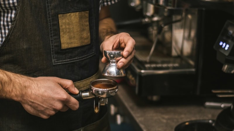 Ein Barista glättet die gemahlenen Bohnen im Siebträger.