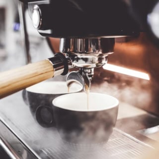 Kaffee läuft aus dem Siebträger in zwei Tassen.