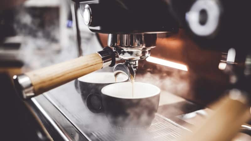 Kaffee läuft aus dem Siebträger in zwei Tassen.