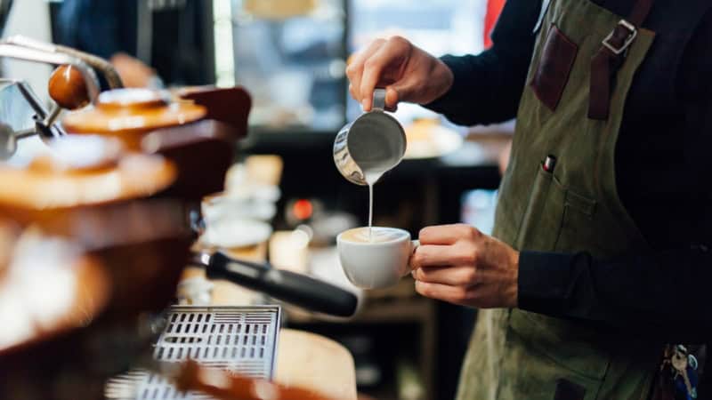 Ein Barista schüttet aufgeschäumte Milch in einen Kaffee.