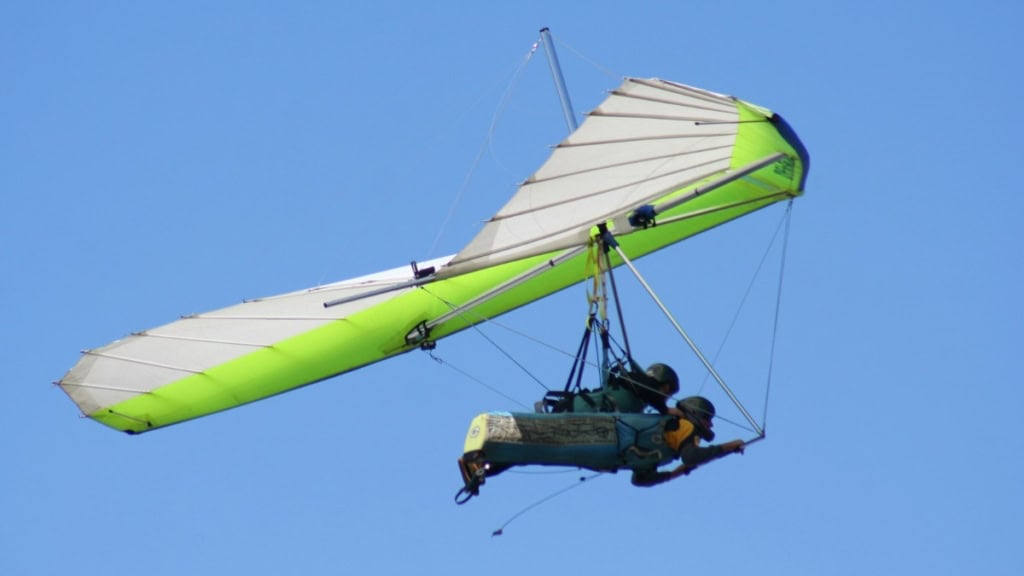 drachen-tandemflug Ein grüner Drachen mit 2 fliegenden wird von hinten fotografiert.