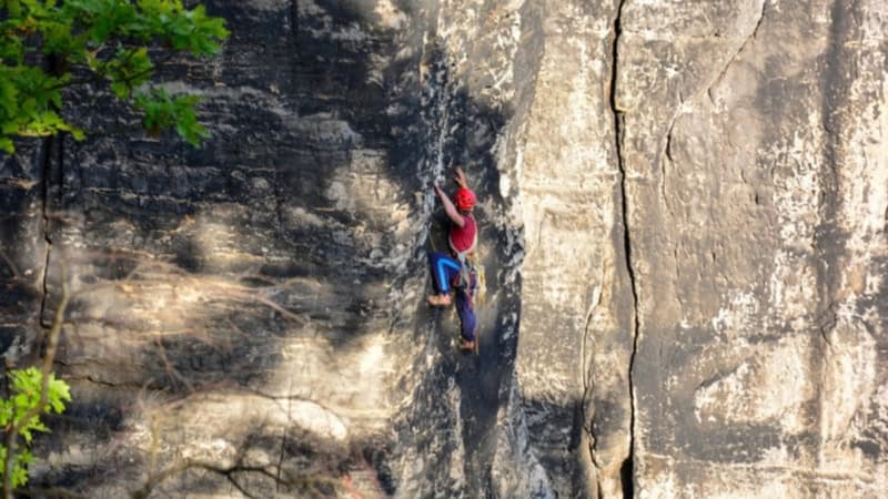 Ein Bergsteiger klettert eine flache Sandstein Felsenwand hoch.